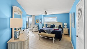 A bedroom with a bed, bedside tables, a bench, a dresser, a mirror, and a ceiling fan. - Xanadu II 605-3BR/3BA Oceanfront condo in Cherry Grove (North Myrtle Beach)