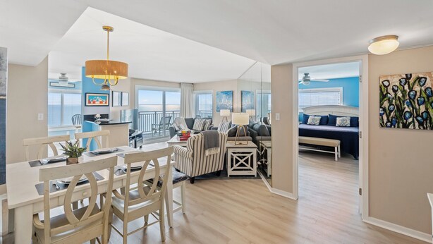 A spacious living area with a dining table, striped armchair, and a view of the balcony. - Xanadu II 605-3BR/3BA Oceanfront condo in Cherry Grove (North Myrtle Beach)