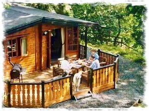 A wooden cabin with a porch, a dining table, and chairs. - Blelham Tarn (Rustic yet modern cabin in tranquil woodland with own EV charger) (Ambleside)