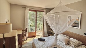 A bedroom with a bed, a desk, and a chair. There is a window with curtains and a view of greenery outside. - Beautiful villa with sea view, 2.5km from the beach, in the heart of nature   (Bormes-les-Mimosas)
