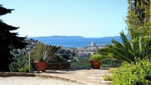 A pathway leading to a terrace with potted plants and a view of a coastal town. - Beautiful villa with sea view, 2.5km from the beach, in the heart of nature   (Bormes-les-Mimosas)