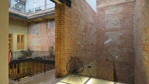 Une cour intérieure avec des murs en briques apparentes, une rambarde en métal et une chaise.