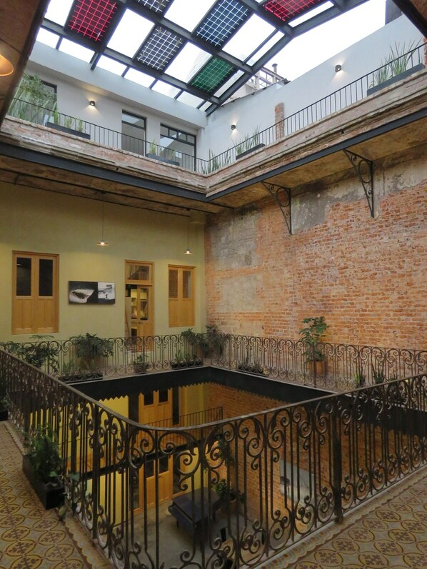 A multi-level atrium with a central courtyard, featuring a brick wall, metal railings, and potted plants.