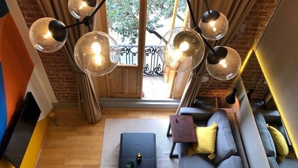 Un salon moderne avec un plafond en bois, un canapé noir avec des coussins, une petite table et un téléviseur.