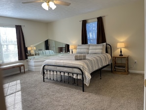 A bedroom with a bed, bedside tables, a bench, a ceiling fan, and a window with curtains.