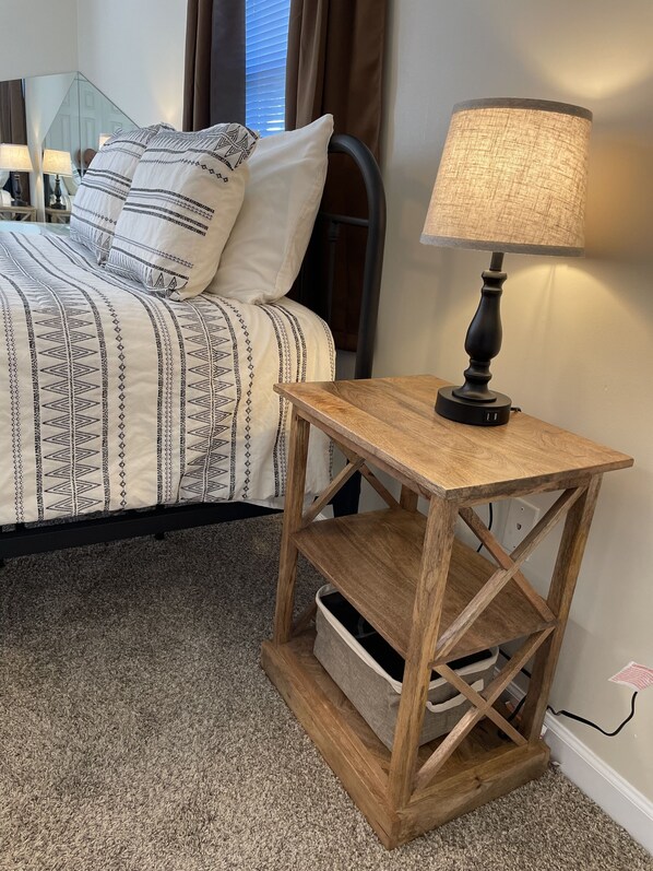 A neatly made bed with patterned bedding, a wooden nightstand with a lamp, and a carpeted floor. - Matthew Estates Ranch (Dandridge)