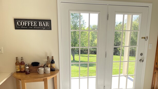 A room with a coffee bar sign, a wooden table with coffee mugs and bottles, and a view of a green lawn through double doors. - Matthew Estates Ranch (Dandridge)