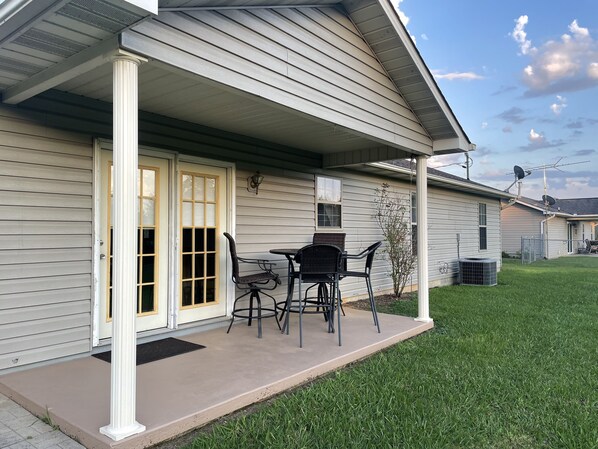A house with a covered porch, a small table with chairs, and a door with glass panels.