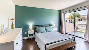 A bedroom with a bed, nightstands, a desk, and a view of the outside. - Sunny Beachside Retreat: Cozy 2 bed Townhouse! (Indialantic)