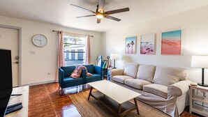 A living room with a ceiling fan, a clock, a TV, two sofas, a coffee table, and a window with curtains. - Sunny Beachside Retreat: Cozy 2 bed Townhouse! (Indialantic)