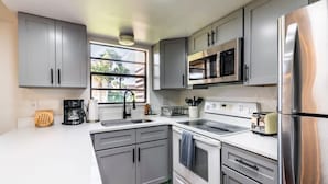A modern kitchen with grey cabinets, stainless steel appliances, and a window providing natural light. - Sunny Beachside Retreat: Cozy 2 bed Townhouse! (Indialantic)