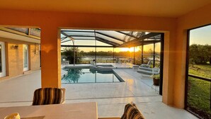 A modern outdoor patio with a pool, seating, and a view of the sunset.