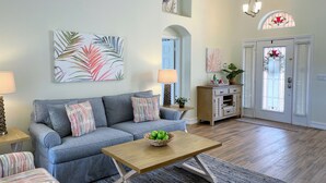 A living room with a sofa, a coffee table with a fruit bowl, and a door with a stained glass window.