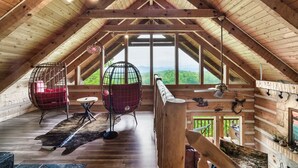 Ruime zolderkamer met houten balken, grote ramen en twee rode eierstoelen.