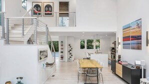 A modern interior with a staircase, dining area, kitchen, and a large window providing natural light. - Contemporary retreat on 1.4 wooded acres with an open floorplan and private... (East Hampton)