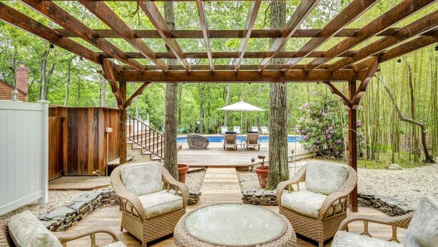 A wooden pergola over a deck with wicker furniture and a pool in the background. - Contemporary retreat on 1.4 wooded acres with an open floorplan and private... (East Hampton)
