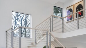 A modern interior with a staircase leading to a second floor, large windows, and framed artwork on the walls. - Contemporary retreat on 1.4 wooded acres with an open floorplan and private... (East Hampton)
