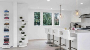 A modern kitchen with white cabinetry, a bar area with white stools, and a bookshelf filled with books. - Contemporary retreat on 1.4 wooded acres with an open floorplan and private... (East Hampton)