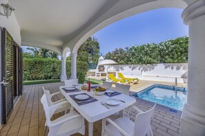 An outdoor dining area with a pool, white furniture, and a barbecue.