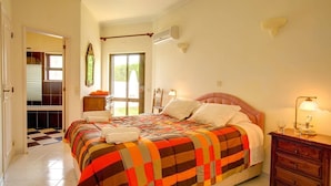 Quarto com uma cama, penteadeira, luminária e vista através de uma porta.