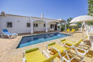 A poolside area with a swimming pool, sun loungers, and a covered seating area.