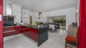 Uma cozinha moderna com ilha central, armários vermelhos e área de refeições com mesa e cadeiras.
