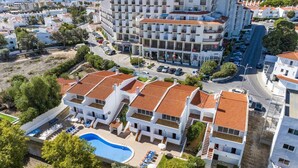 Um hotel com vários andares, piscina e área externa com mesas e cadeiras.