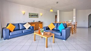Uma sala de estar com dois sofás azuis, uma mesa de centro de madeira e uma área de jantar com uma mesa e cadeiras de madeira.
