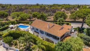 Una casa de dues plantes amb piscina, envoltada de vegetació abundant i arbres.