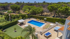 Zona de piscina amb una piscina rectangular, gandules, una taula amb caires i una taula de ping-pong.