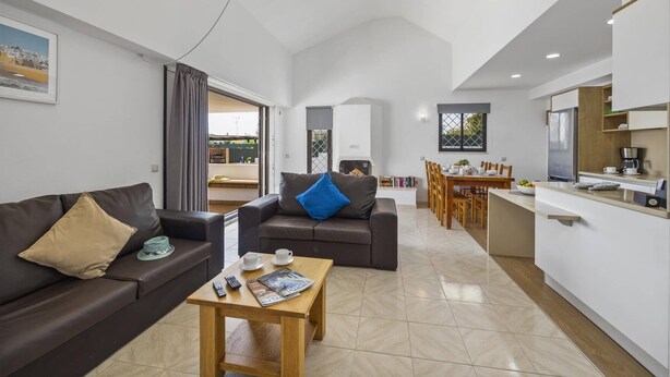 A modern living room with a sofa, a coffee table, and a dining area with a table and chairs. - Villa Amendoeira by Villa Plus (Albufeira)