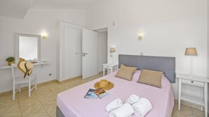 A bedroom with a bed, two bedside tables, a nightstand, a wardrobe, a mirror, and a window. - Villa Amendoeira by Villa Plus (Albufeira)