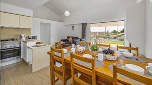 A modern kitchen with a stove, sink, and dining area with wooden chairs and a table set for four. - Villa Amendoeira by Villa Plus (Albufeira)