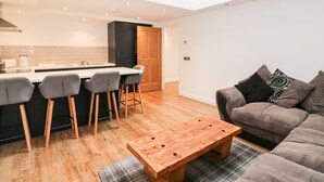 Een moderne keuken met een centraal eiland, barkrukken, een houten salontafel en een bank met decoratieve kussens.