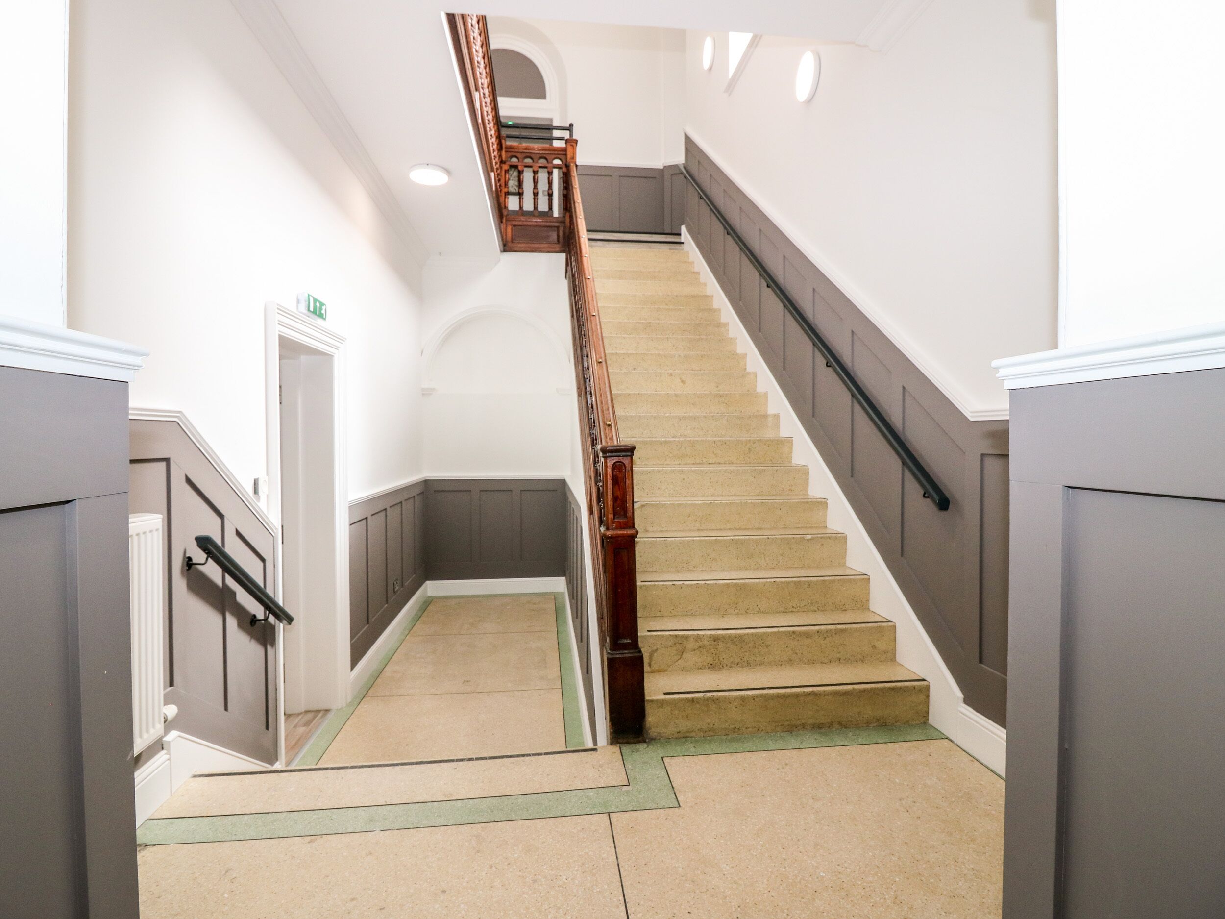 A staircase with a wooden handrail and beige steps, leading to an upper floor.