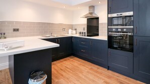 A modern kitchen with dark cabinetry, a white countertop, and built-in appliances. - The Court Room at The Institute Executive Apartments (Keith)