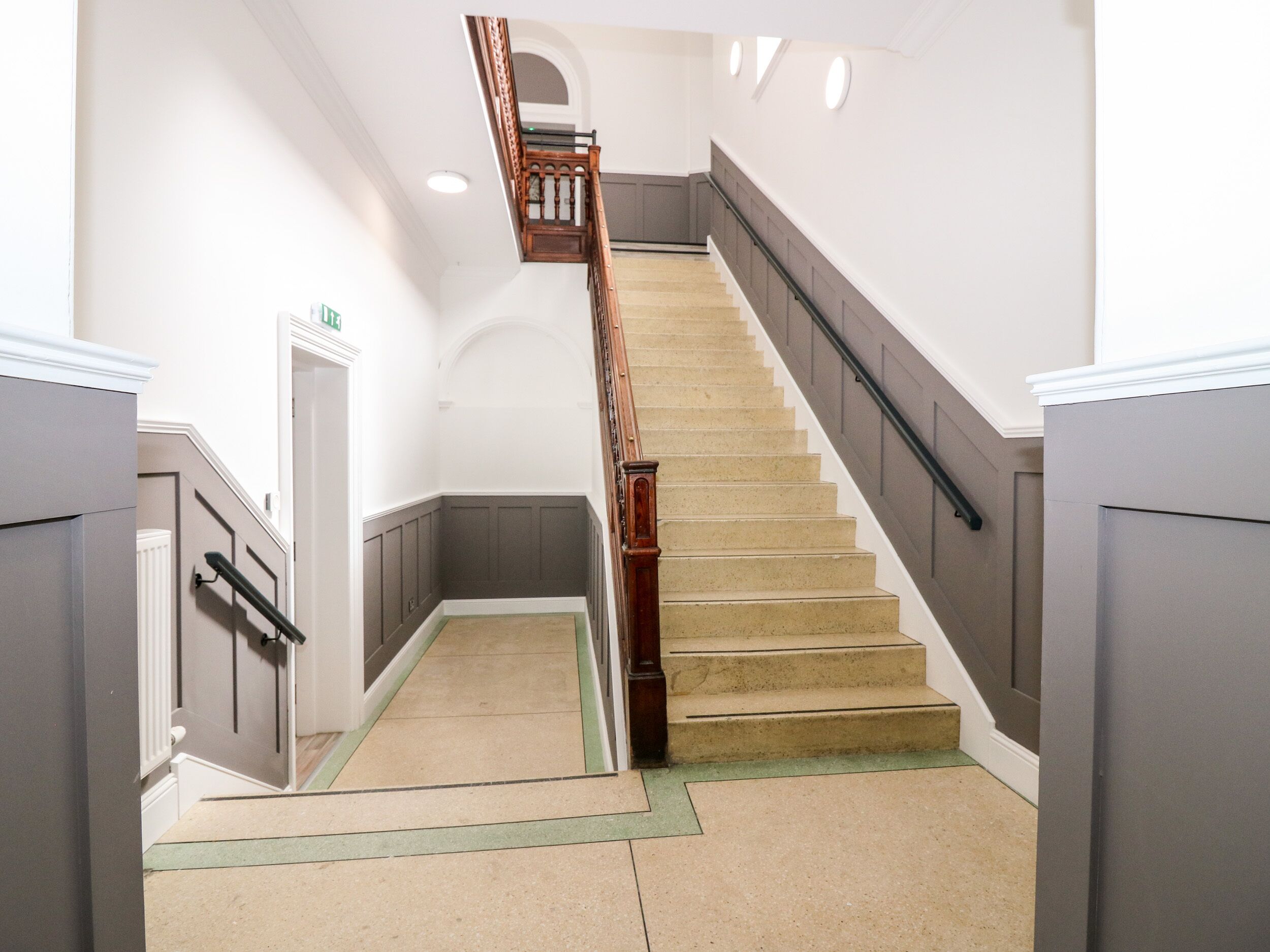 A modern staircase with a wooden handrail and beige carpeted steps.