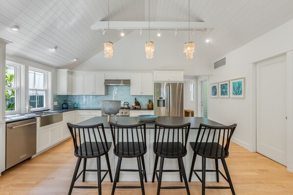 A modern kitchen with white cabinets, a central island with bar stools, stainless steel appliances, and pendant lighting.