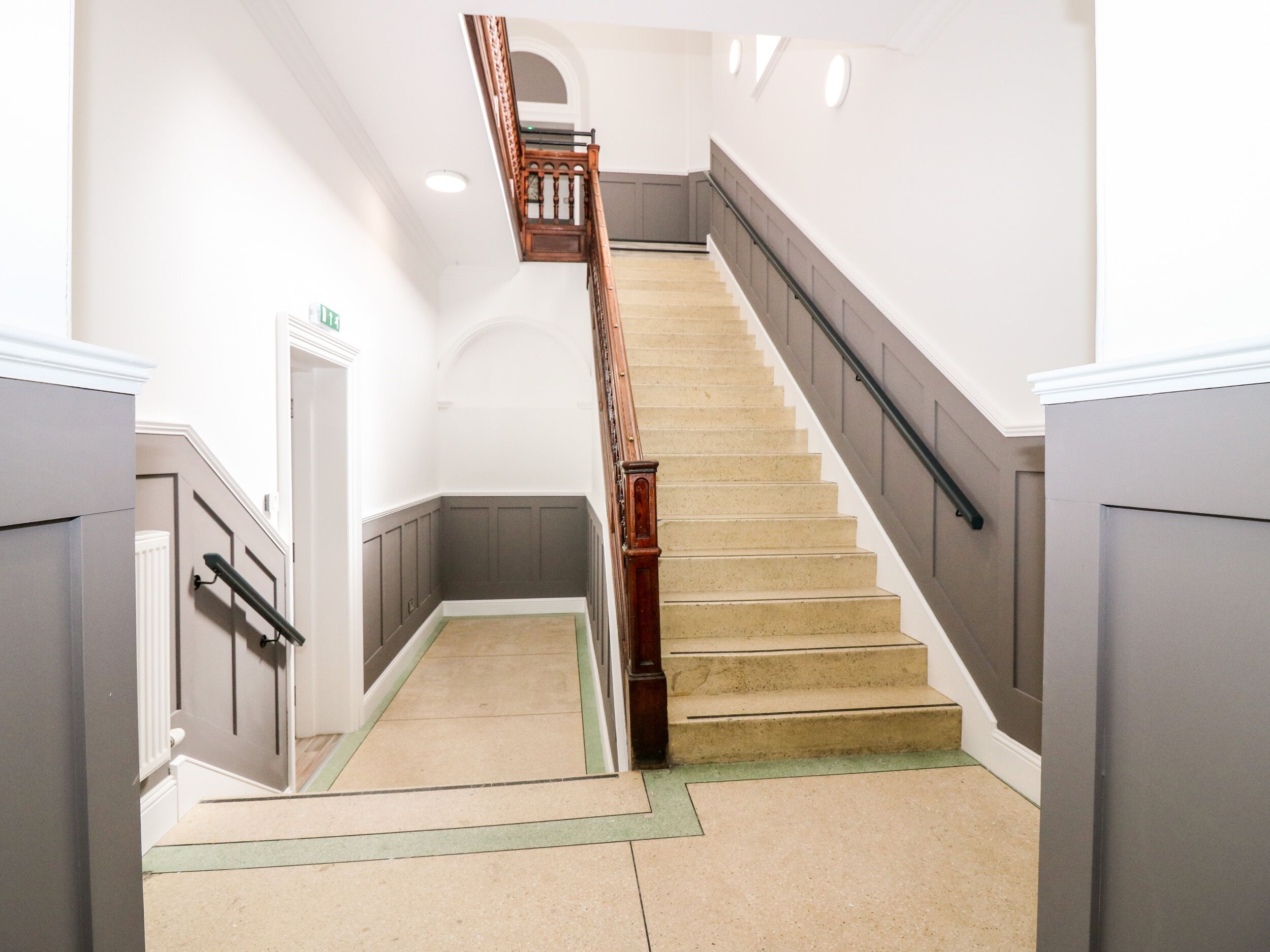 A staircase with a wooden handrail and beige steps, leading to an upper floor.