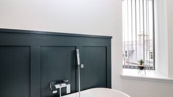 Un bagno moderno con una vasca freestanding, una parete rivestita in legno scuro e una finestra con vista sugli edifici.