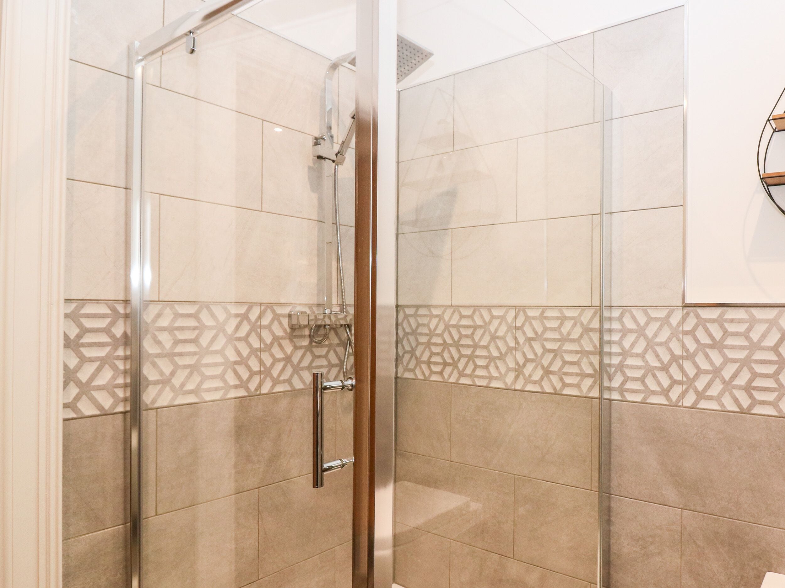 A glass-enclosed shower with a geometric tile pattern on the lower half of the walls.