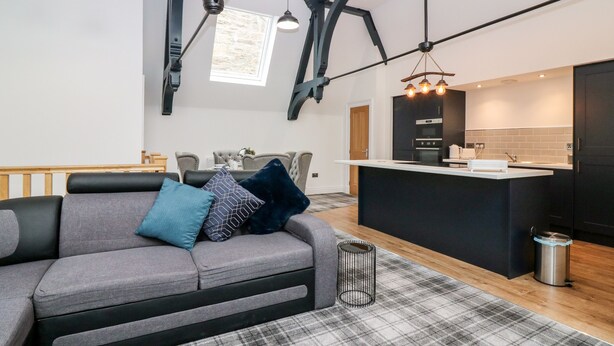 Ein modernes Wohnzimmer mit einem grauen Sofa, gemusterten Kissen und einem karierten Teppich.