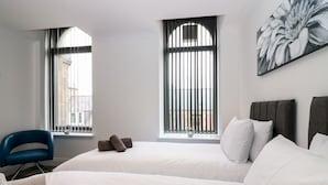 Ein Hotelzimmer mit zwei Betten, einem blauen Sessel und einem großen Fenster mit Blick auf Gebäude.