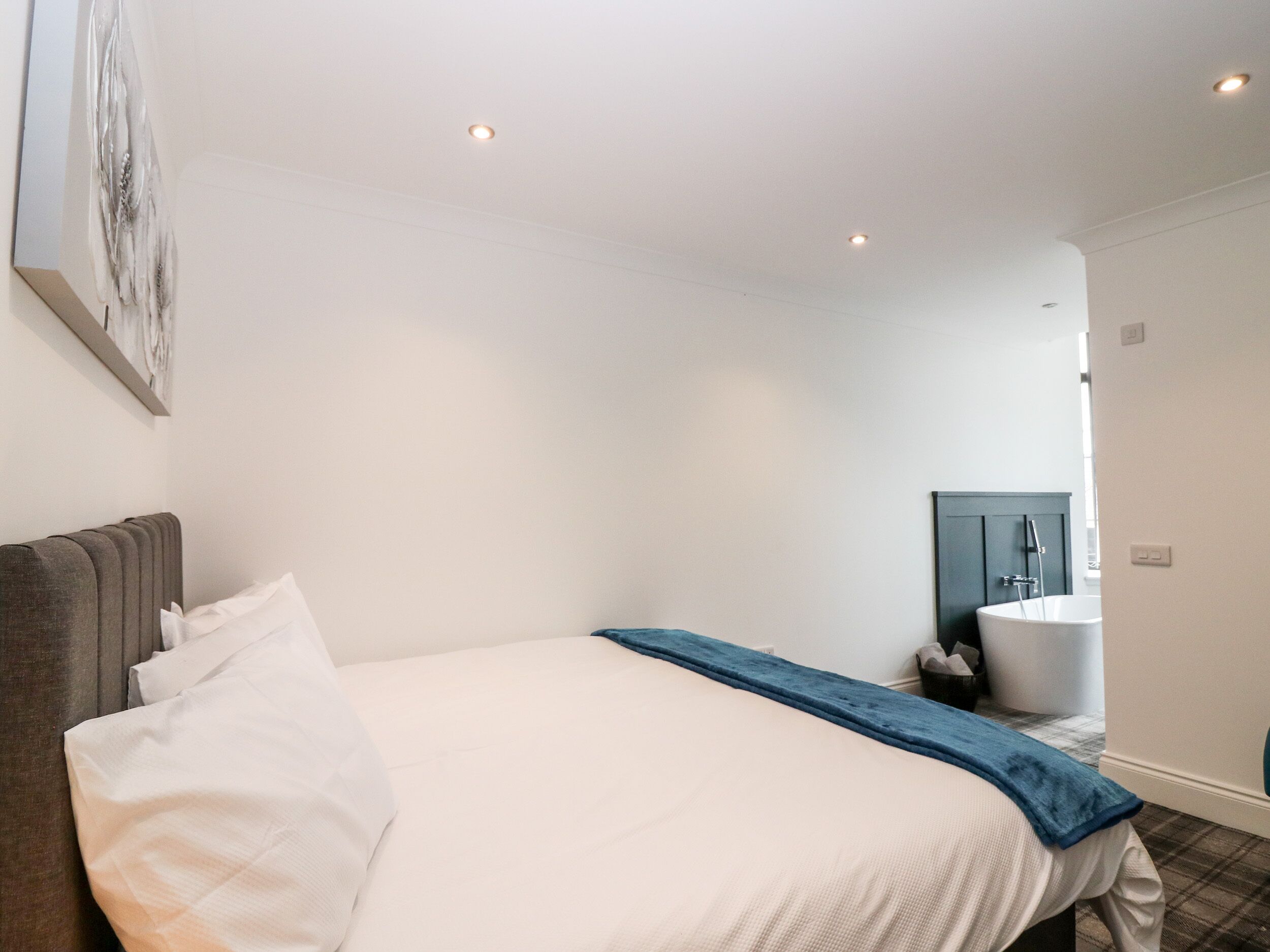 A bedroom with a bed, a headboard, a blue throw blanket, and a bathroom visible through an open door.