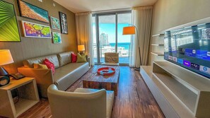 A hotel room with a large TV, a sofa, a coffee table, and a view of the city.