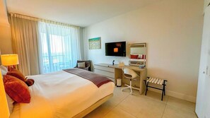 Habitación de hotel con una cama grande, un escritorio, una silla, un televisor y una ventana con cortinas.