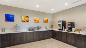A modern kitchen area with dark cabinets, a white countertop, and various appliances. There are three wall-mounted pictures depicting fruits and a blue sign with the text "RISE & SHINE". - Comfort Inn & Suites Balch Springs - SE Dallas (Mesquite)
