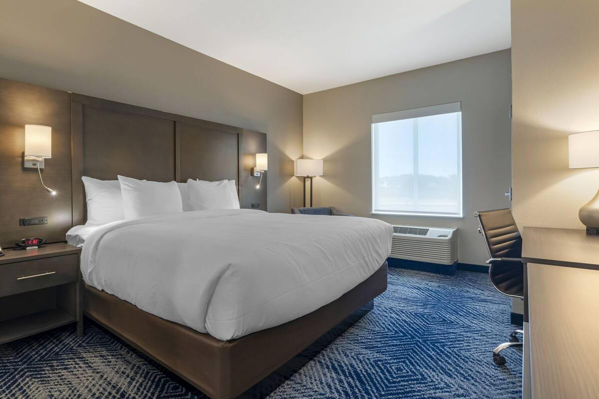 A hotel room with a large bed, bedside tables, a desk, and a window.