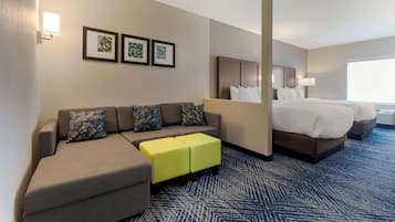 Una habitación de hotel con sofá, dos otomanos amarillos, cama y un ventanal grande.