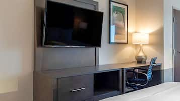 Habitación de hotel con televisión de pantalla plana montada en la pared, escritorio con silla, lámpara y cama.